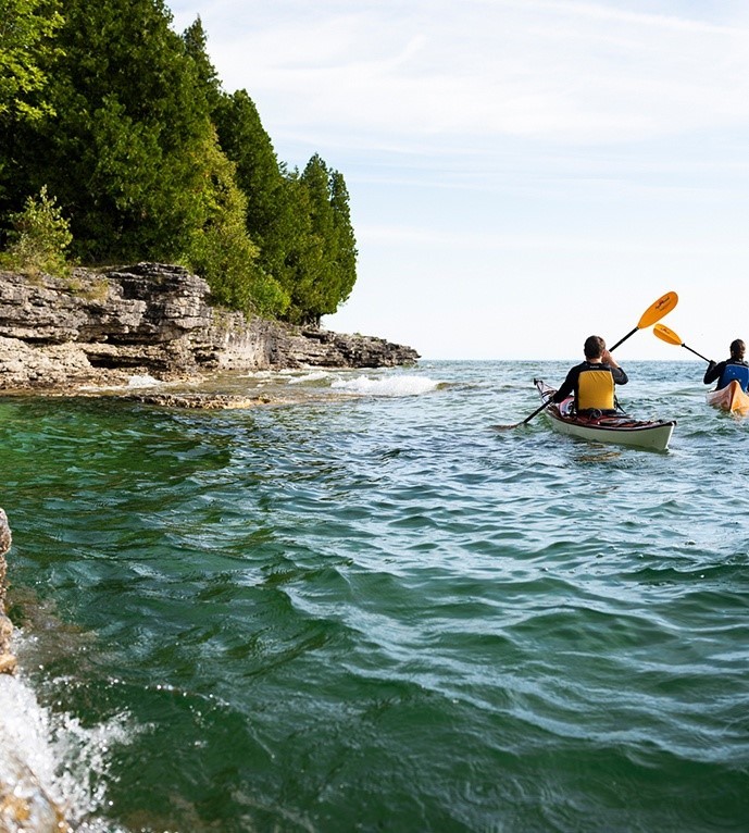 Two people kayaking along the shoreline.