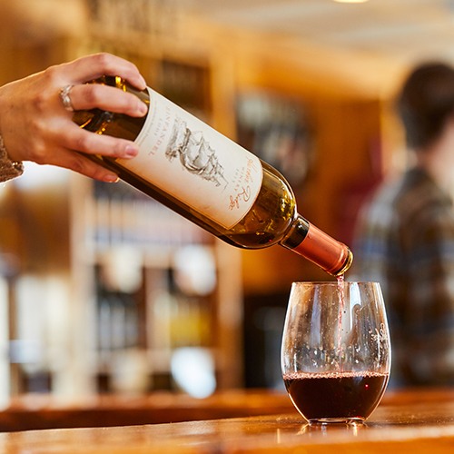 A bartender pours red wine into a stemless glass.