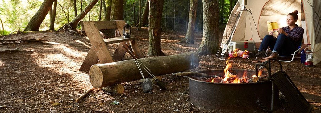 A woman reading a book at a campsite.