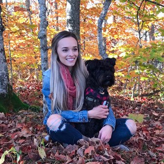 A woman sitting with a dog in the leaves.