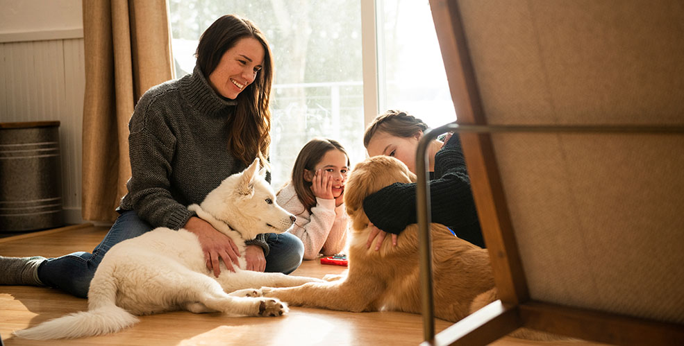 A woman and kids laying on the floor with two dogs.