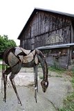 A metal sculpture of a horse in front of a barn.