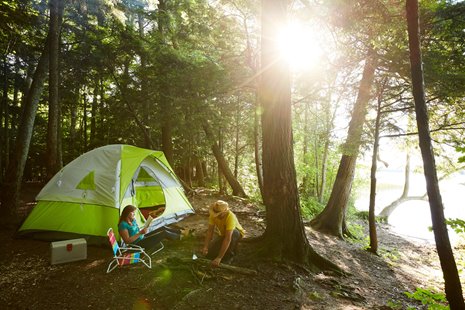 Sun shining through the trees with a couple at their campsite near a tent