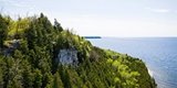 A person standing at the top of a tree-lined cliff looking out at the lake.