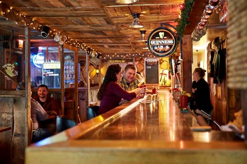 A couple drinks and dines at a bar in a wood-outfitted restaurant.