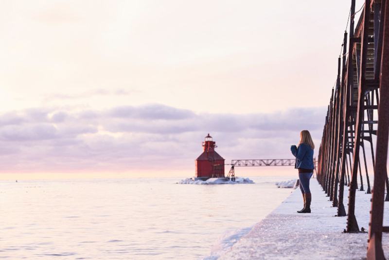 Woman standing in the snow by pier with a red lighthouse in the background