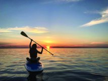 Person sitting on a paddle board floating on the lake at sunrise.