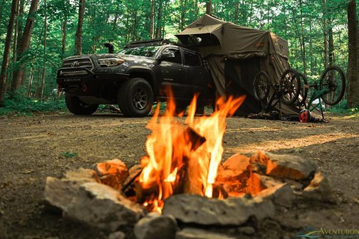 A campfire with a tent and mountain bike in the background.