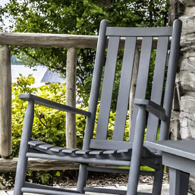 An old rocking chair sits on an outdoor porch on a summer day.