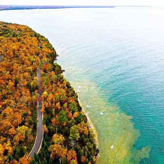 A road surrounded by trees in their autumn colors near the lake.