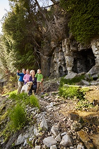 A family with a dog hiking outside of a cave.