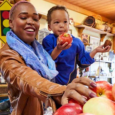 A woman holding her child while picking an apple at a market