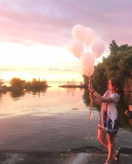 Woman with white balloons at the lakefront.