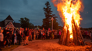 Large crowd gathered around big wood fire