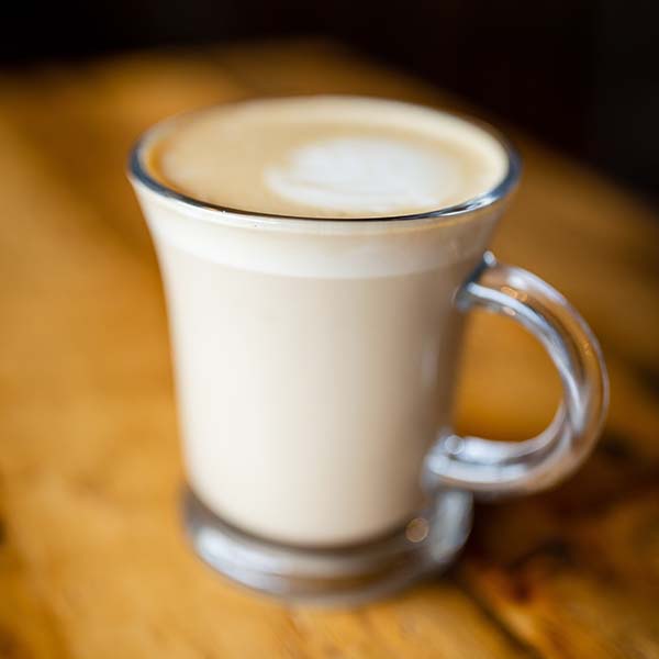 A latte sits on a wooden table.