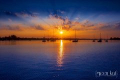 The sun setting over the lake beyond a group of sailboats.