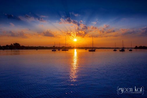 The sun setting over the lake beyond a group of sailboats.