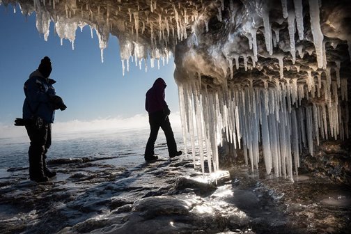 People hiking outside an ice-covered cave.