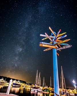 Looking up at a sign post with signs pointing in many directions against a starry night sky.