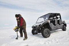 A man drilling a hole in the ice in front of an ATV