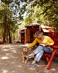 A woman sitting in a chair leaning forward to pet a dog.