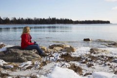 A woman sitting on a rock at the snow-covered lakefront.