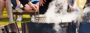 Person dipping a metal basket into a boiling pot.