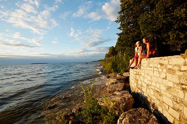 People sitting on a wall near the water enjoying the sunset