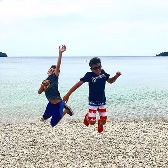 Two boys jumping into the air at the lakefront.