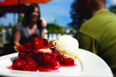 A plate of cherry pie with ice cream with people dining in the background.