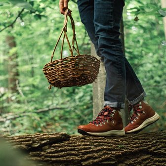 Closeup of a person walking across a fallen log holding a basket.